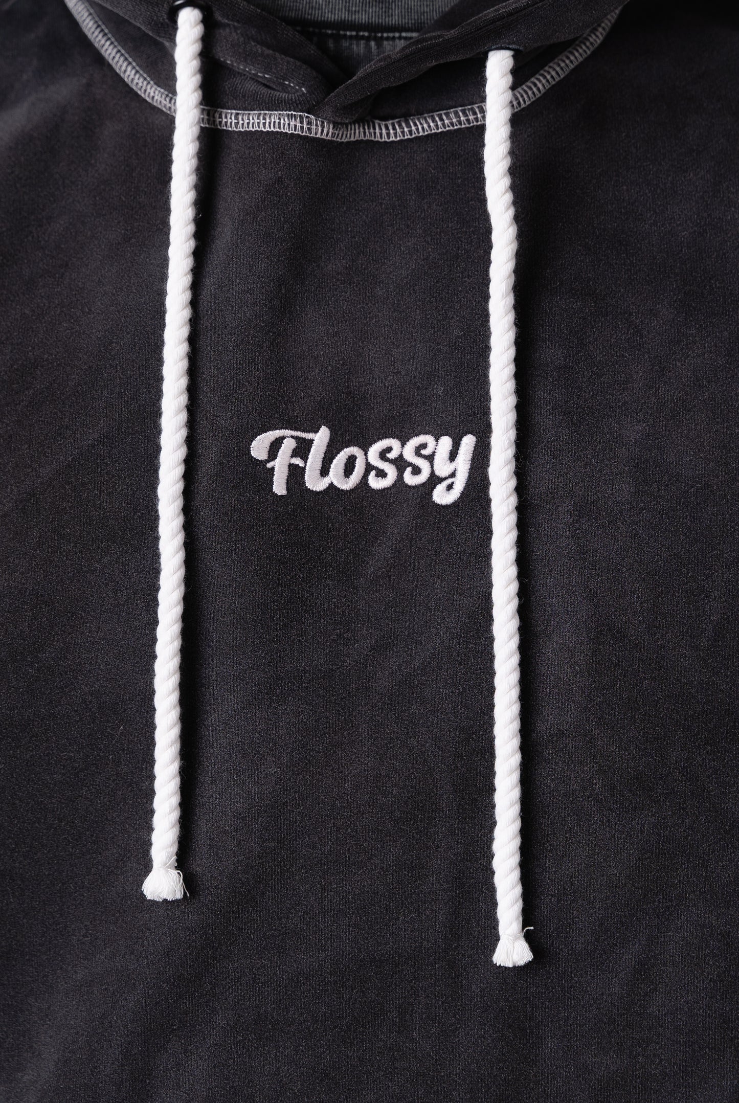 Closeup of tonal embroidered Flossy logo at chest on acid wash black hoodie