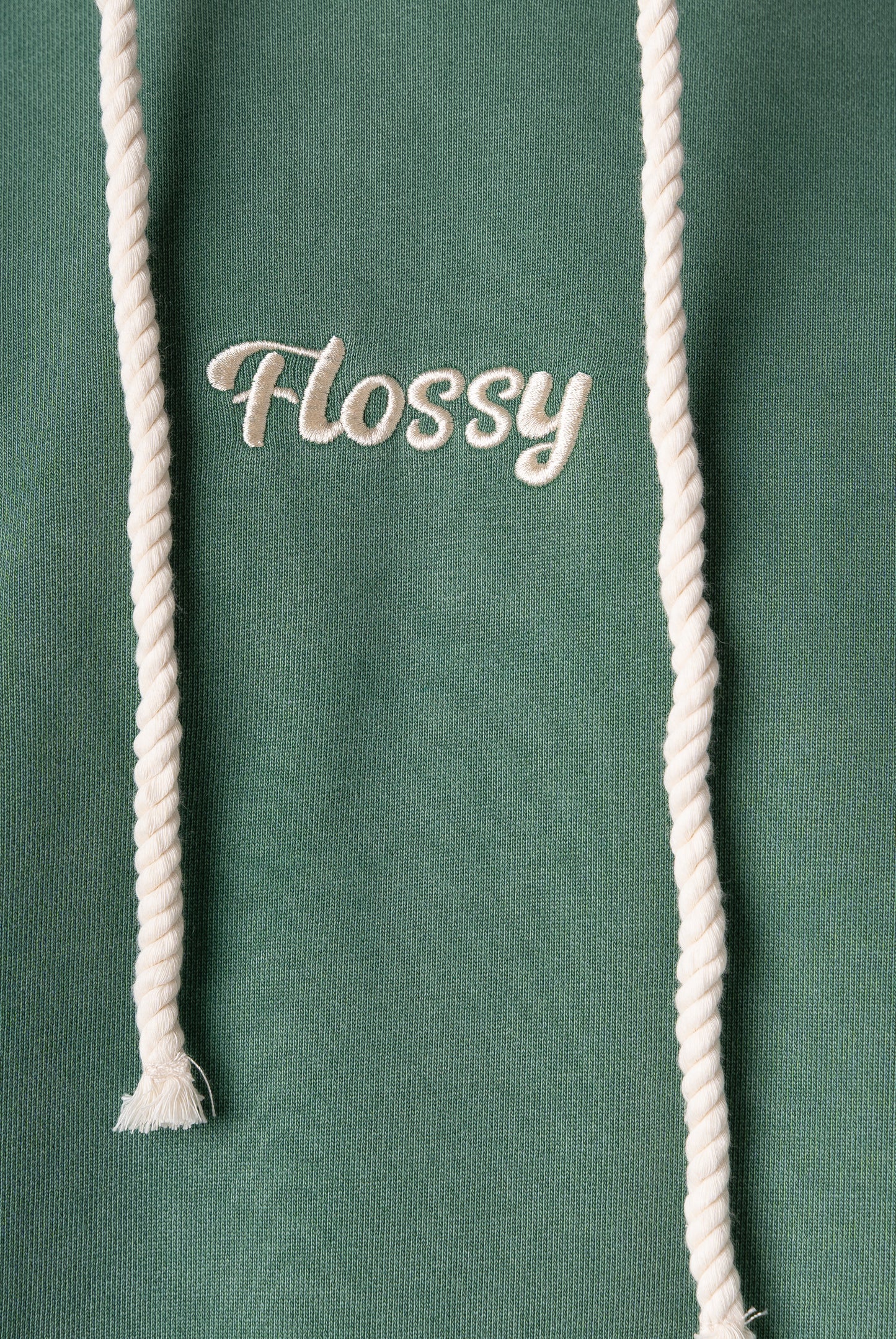Closeup of tonal embroidered Flossy logo at chest on acid wash green hoodie