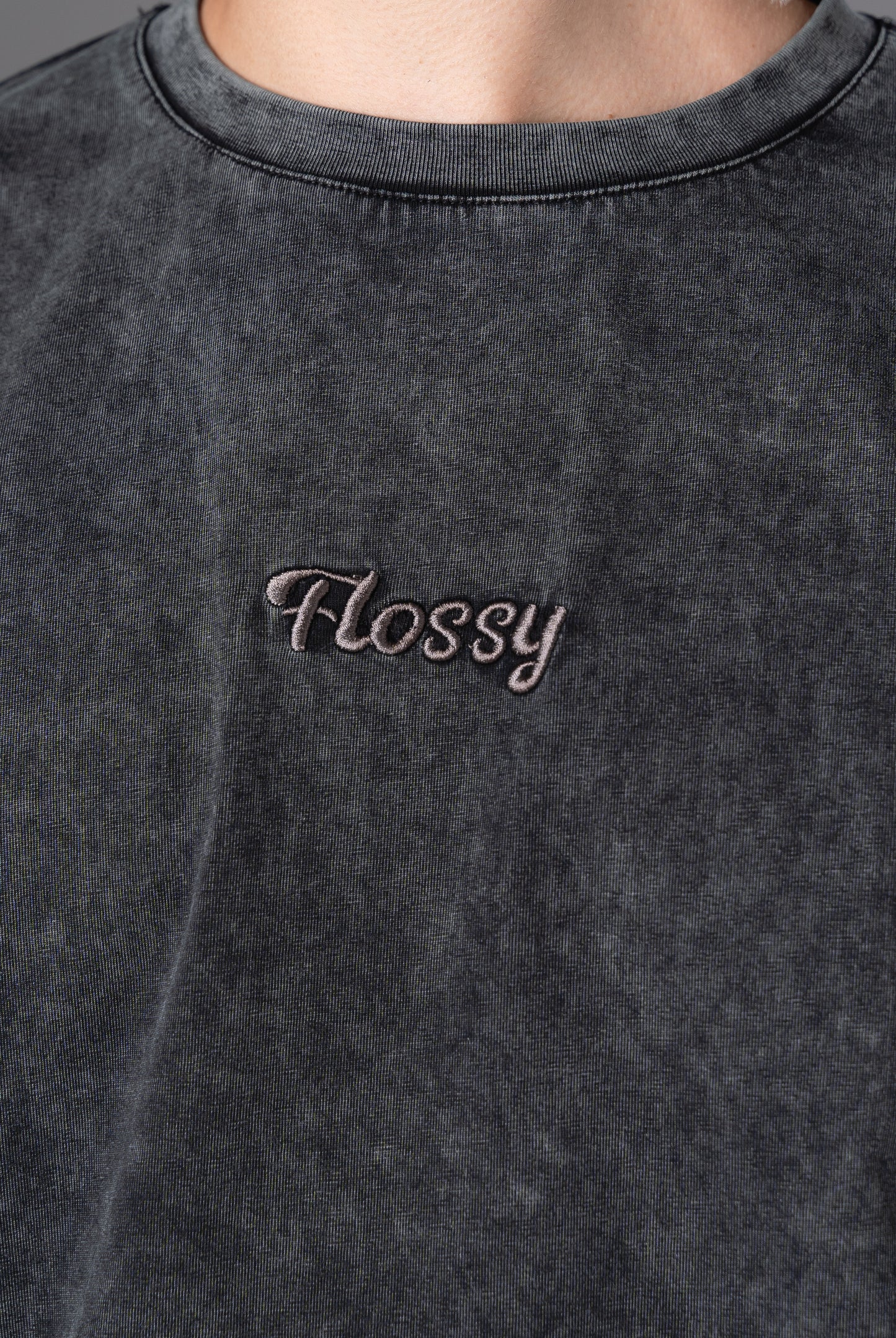 Closeup of tonal embroidered Flossy logo at chest on acid wash black tee