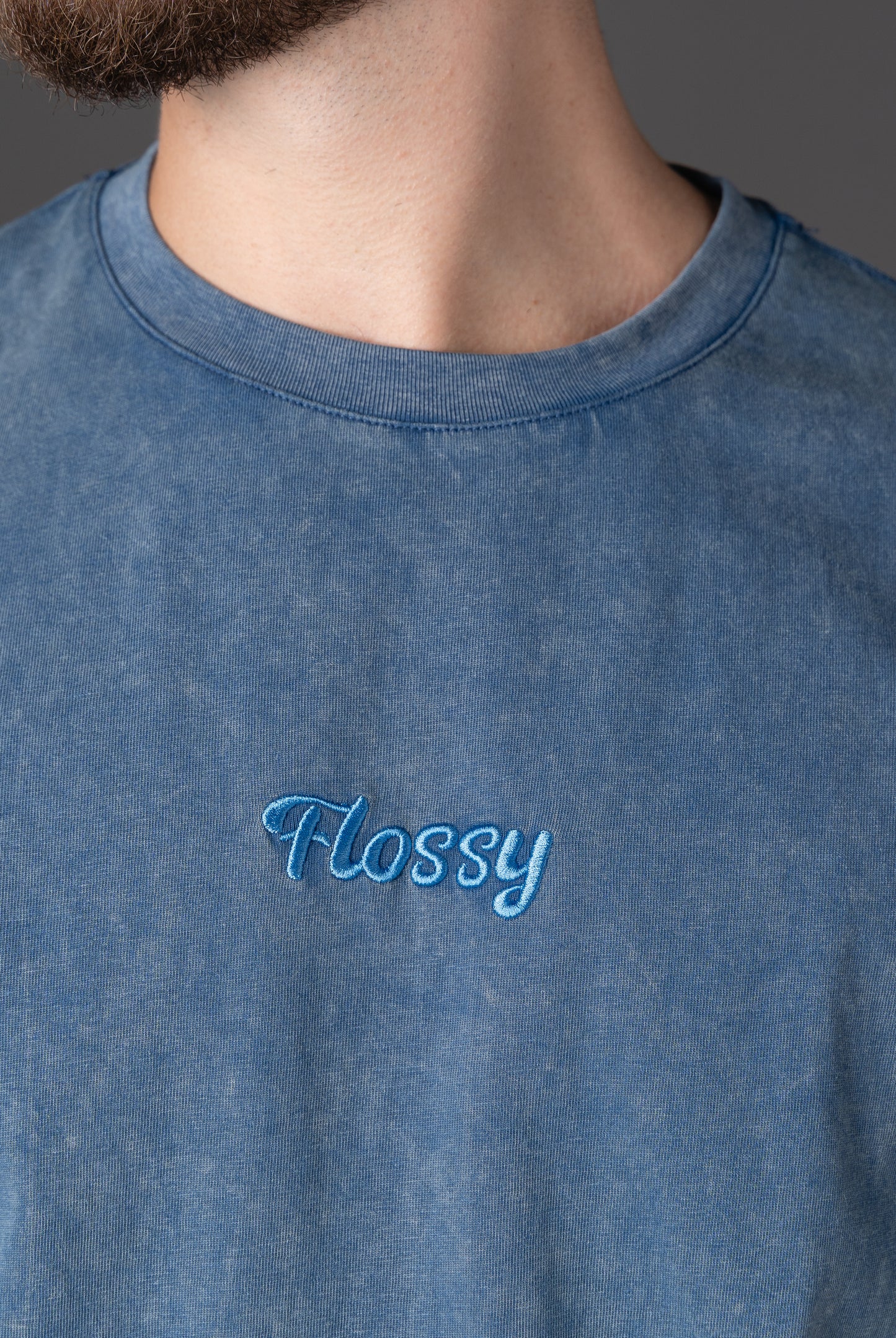 Closeup of tonal embroidered Flossy logo at chest on acid wash blue tee